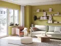 Jasnozielone kolory ścian do salonu tworzą przytulną atmosferę. Wygodna sofa i fotel zapraszają do relaksu.