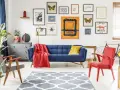 Salon w stylu eklektycznym: granatowa kanapa, czerwone fotele, galeria obrazów z motywami natury i abstrakcji, szara komoda, dywan z geometrycznym wzorem.