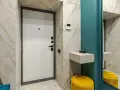 Mały przedpokój w bloku: inspiracje. Marmurowe płytki, turkusowa ściana i żółty puf tworzą stylowe wnętrze.