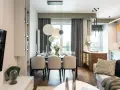 Elegancka jadalnia z nowoczesnym stołem i krzesłami. W tle kuchnia z drewnianymi elementami i subtelnym akcentem w kolorze pistacjowym.