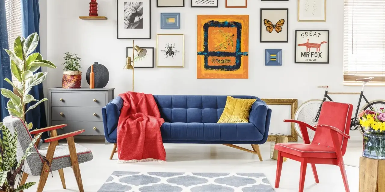 Salon w stylu eklektycznym: granatowa kanapa, czerwone fotele, galeria obrazów z motywami natury i abstrakcji, szara komoda, dywan z geometrycznym wzorem.
