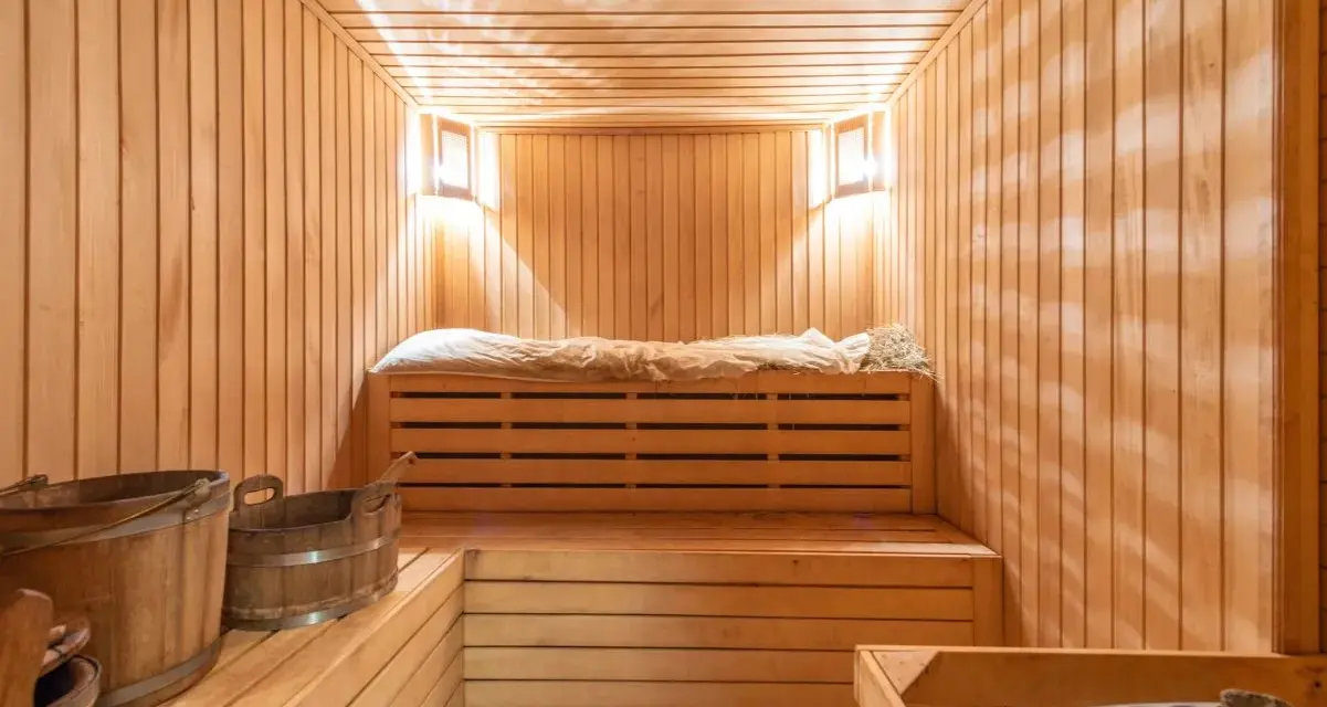 Przytulna sauna w domu, z drewnianymi ławami, wiaderkami i kamiennym piecem. Idealne miejsce na relaks.