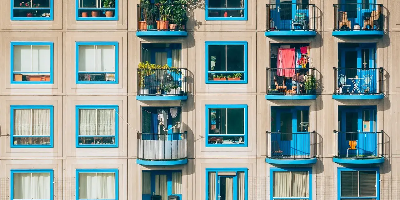 Elegancka loggia i balkon z niebieskimi ramami okiennymi, pełne zieleni i suszącego się prania, tworzą kolorowy kontrast na betonowej fasadzie.