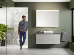 Nowoczesna wizualizacja łazienki z mężczyzną wchodzącym do strefy prysznicowej. Elegancka armatura, lustro z podświetleniem i minimalistyczna szafka pod umywalkę.