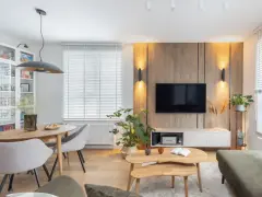 Przytulny salon inspiracje: drewniana ściana z TV, jadalnia, wygodne fotele i stoliki kawowe tworzą ciepłą atmosferę.