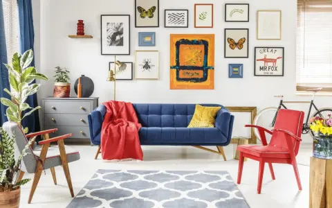 Salon w stylu eklektycznym: granatowa kanapa, czerwone fotele, galeria obrazów z motywami natury i abstrakcji, szara komoda, dywan z geometrycznym wzorem.