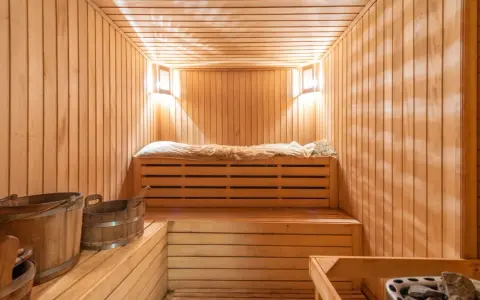 Przytulna sauna w domu, z drewnianymi ławami, wiaderkami i kamiennym piecem. Idealne miejsce na relaks.
