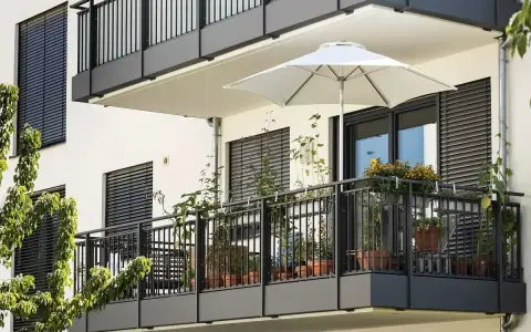 Nowoczesny balkon po remoncie, z białym parasolem i doniczkami pełnymi zieleni.