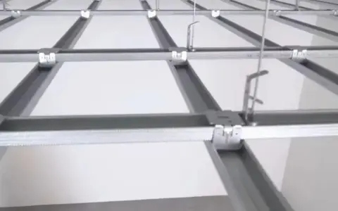 Sufit podwieszany krzyżowy z białymi panelami i metalową konstrukcją. Widać system profili, który tworzy siatkę, a nie pojedyncze belki.