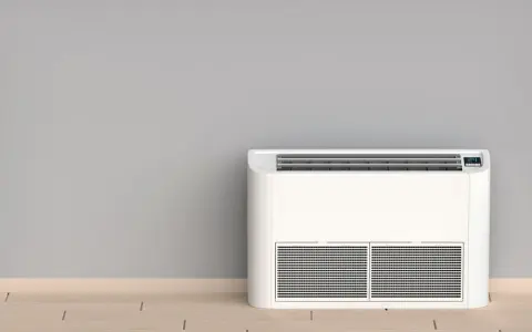Nowoczesny klimatyzator bez jednostki zewnętrznej, stojący na drewnianej podłodze przy szarej ścianie.
