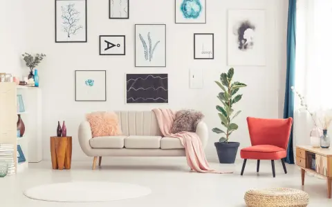 Sofa w kolorze ecru jaki to kolor? Delikatna, przytulna, idealna do salonu. Obok niej czerwony fotel i mnóstwo obrazów na ścianie.