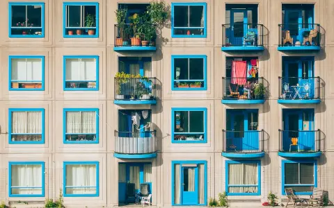 Elegancka loggia i balkon z niebieskimi ramami okiennymi, pełne zieleni i suszącego się prania, tworzą kolorowy kontrast na betonowej fasadzie.