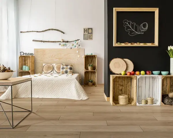 Jak pogodzić salon z sypialnią? Drewniane skrzynki, łóżko z drewnianym zagłówkiem i dekoracje w stylu rustykalnym tworzą przytulną przestrzeń.