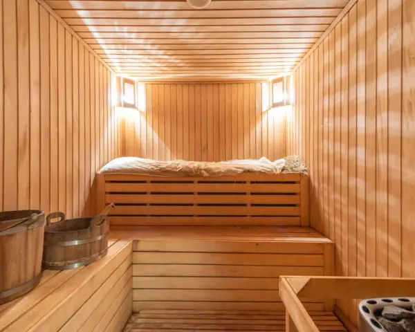 Przytulna sauna w domu, z drewnianymi ławami, wiaderkami i kamiennym piecem. Idealne miejsce na relaks.