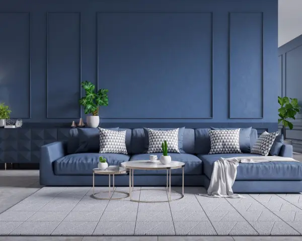 Nowoczesny salon z granatową kanapą, geometrycznymi poduszkami i roślinami.