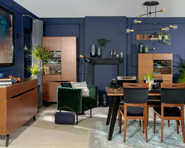 Elegancka jadalnia w odcieniach **kolor navy**. Drewniane meble, aksamitny fotel i nowoczesne oświetlenie tworzą przytulną atmosferę.