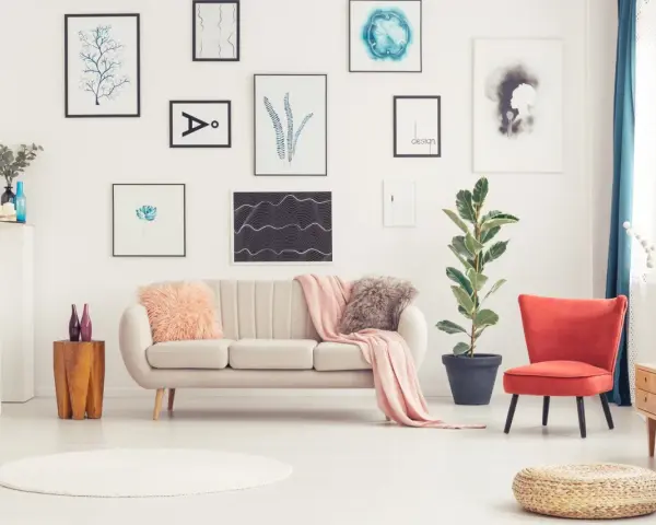 Sofa w kolorze ecru jaki to kolor? Delikatna, przytulna, idealna do salonu. Obok niej czerwony fotel i mnóstwo obrazów na ścianie.
