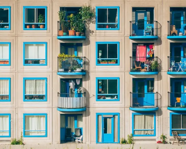 Elegancka loggia i balkon z niebieskimi ramami okiennymi, pełne zieleni i suszącego się prania, tworzą kolorowy kontrast na betonowej fasadzie.
