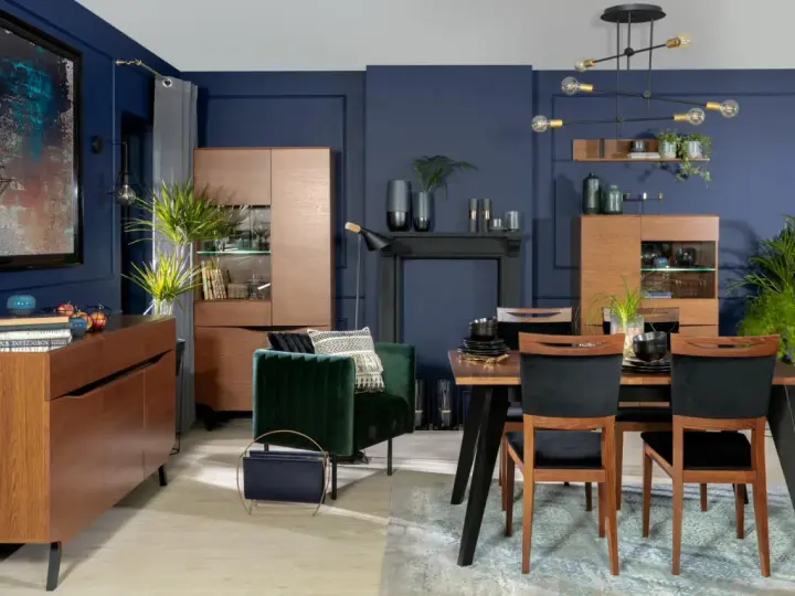 Elegancka jadalnia w odcieniach **kolor navy**. Drewniane meble, aksamitny fotel i nowoczesne oświetlenie tworzą przytulną atmosferę.