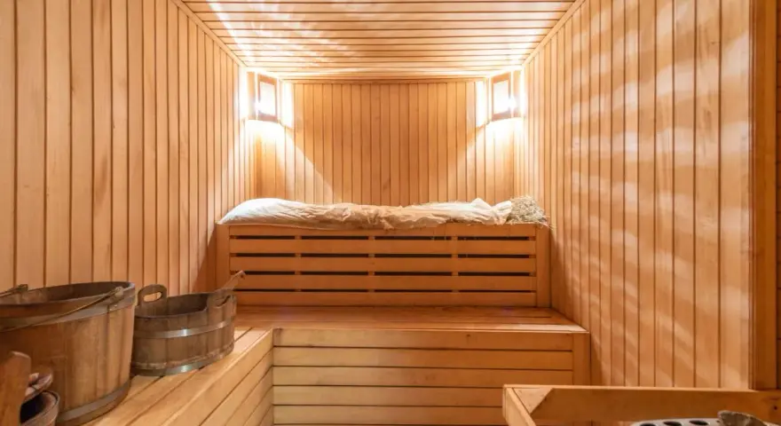 Przytulna sauna w domu, z drewnianymi ławami, wiaderkami i kamiennym piecem. Idealne miejsce na relaks.