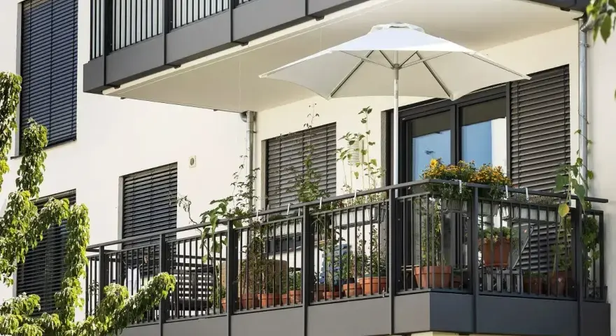 Nowoczesny balkon po remoncie, z białym parasolem i doniczkami pełnymi zieleni.